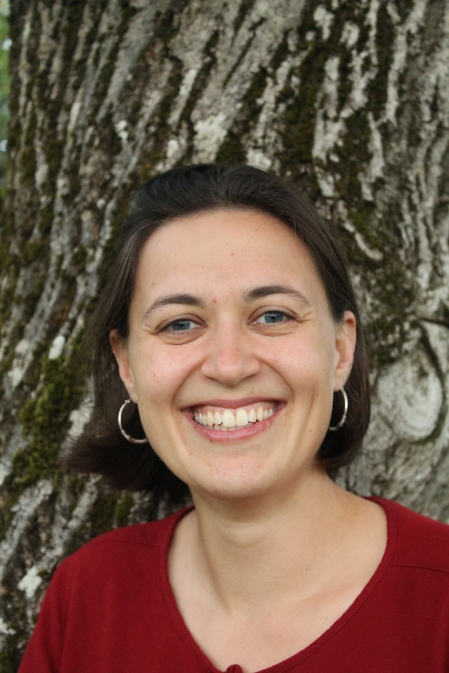 Samira Steck, lächelnd vor einem Baumstamm.